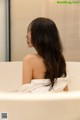 A woman sitting in a bathtub with her back to the camera.