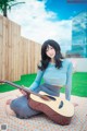 A woman sitting on a blanket holding a guitar.