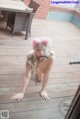 A woman in a pink cat ears headband is posing on a wooden deck.