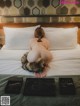 A naked woman sitting on a bed next to a box of jewelry.