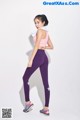 A woman in a pink top and purple leggings posing for a picture.