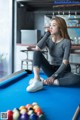 A woman sitting on a pool table next to a pool ball.