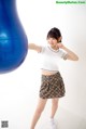 A woman in a white shirt and plaid skirt posing next to a blue ball.