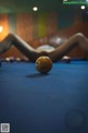 A woman laying on a pool table next to a pool ball.