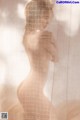 A nude woman standing in front of a sheer curtain.