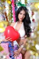 A woman holding a red heart in front of a Christmas tree.