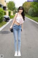 A woman in a pink top and jeans standing on a street.