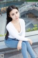 A woman in a white shirt and blue jeans sitting on a ledge.